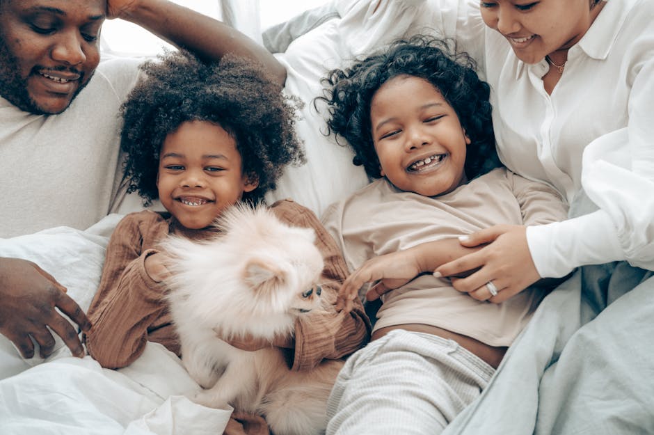 Adorable little ethnic girls having fun while lying in soft bed with fluffy dog and crop parents