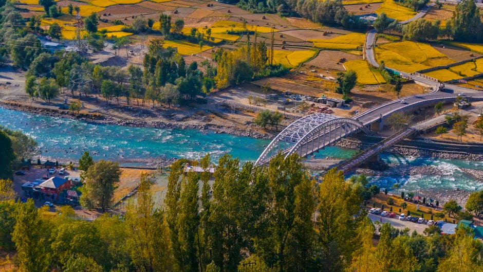 A beautiful aerial view of a bridge over a river surrounded by vibrant autumn fields in Ganderbal.