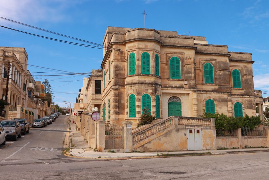 Explore this classic Maltese building with unique green shutters on a sunny urban street corner in Malta.