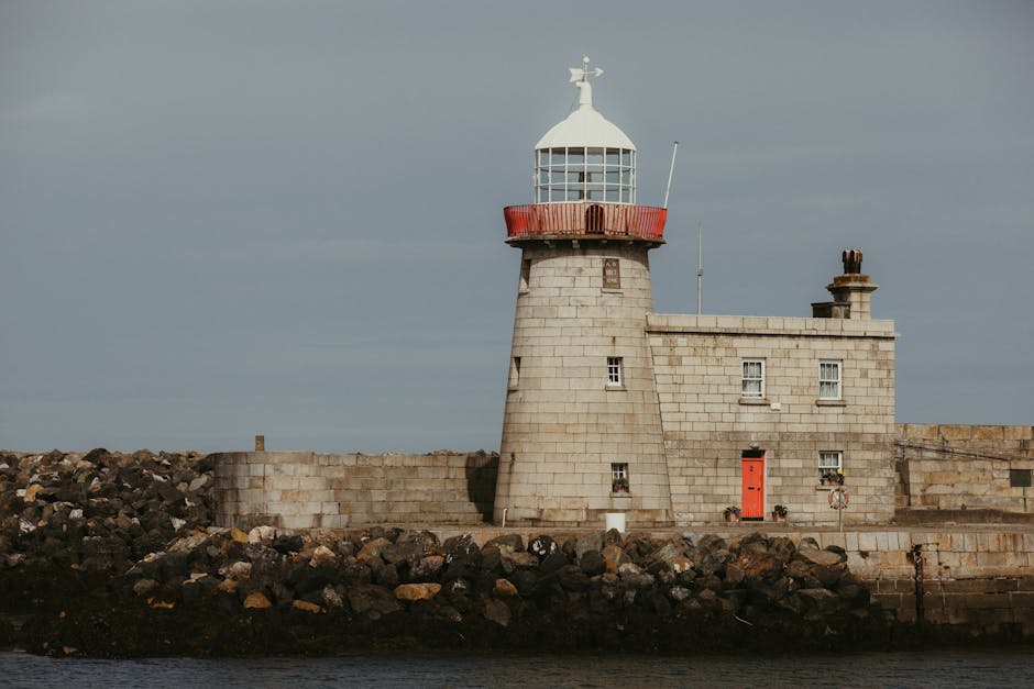 A picturesque view of Howth Harbour Lighthouse in Dublin with rocky foreground and calm water.