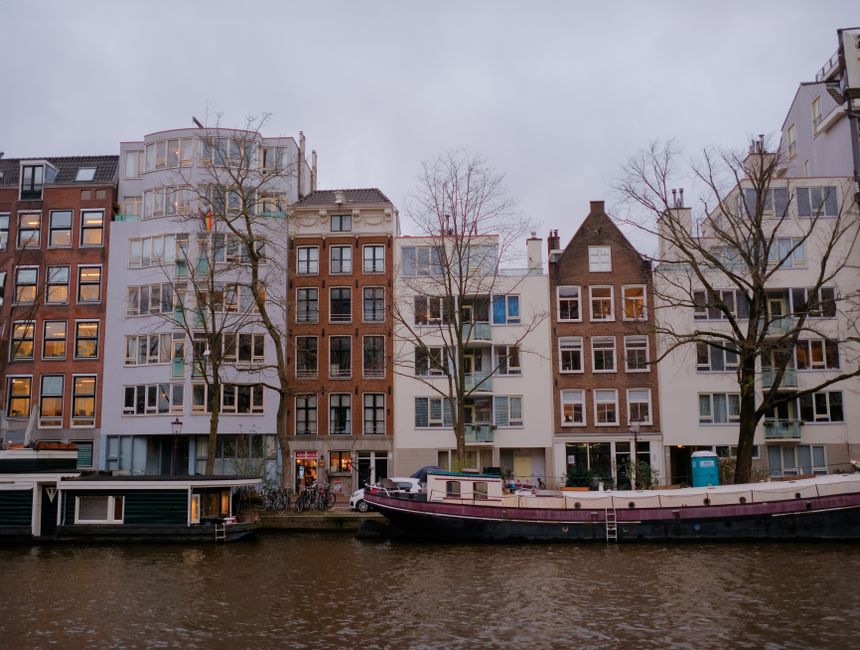 Charming rowhouses along a canal in Amsterdam, featuring boats and winter's bare trees.