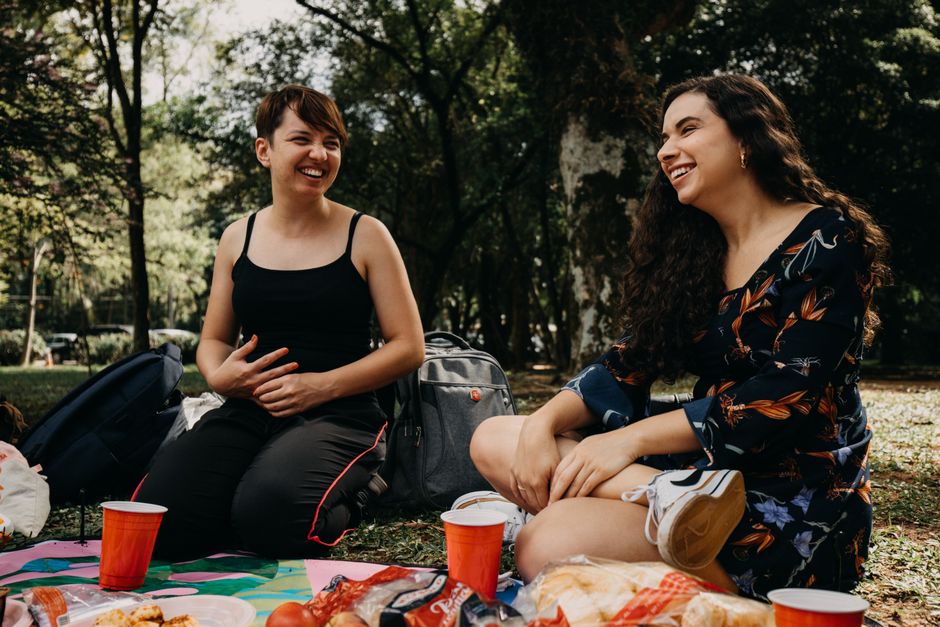 Two women enjoying a lively picnic in a park, surrounded by nature and laughter.