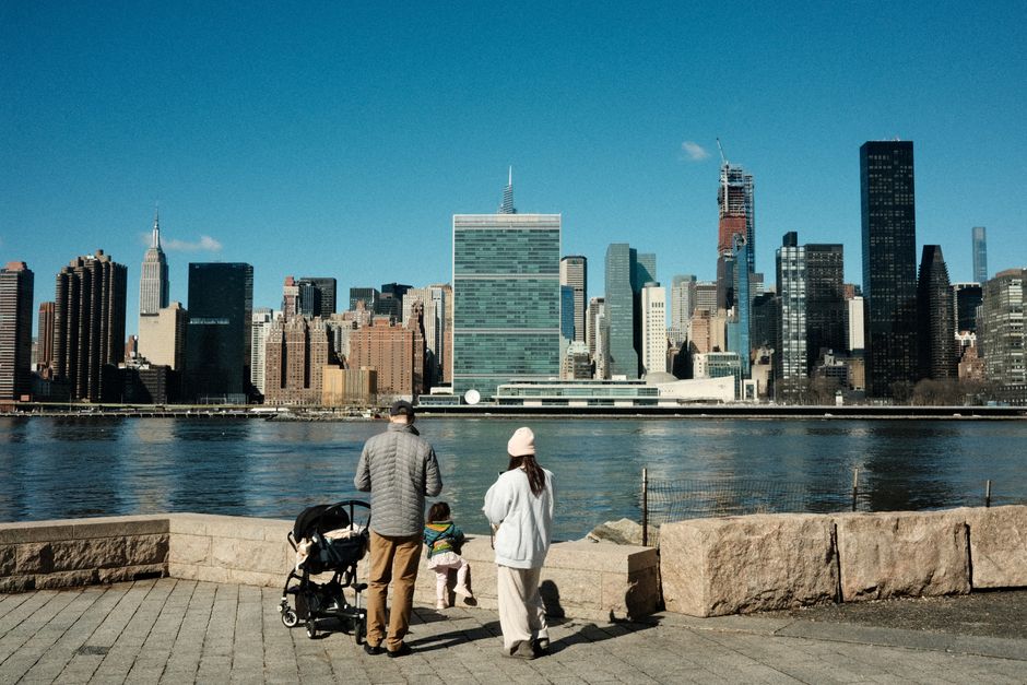 A family enjoys a riverside stroll with New York City's iconic skyline as the backdrop.