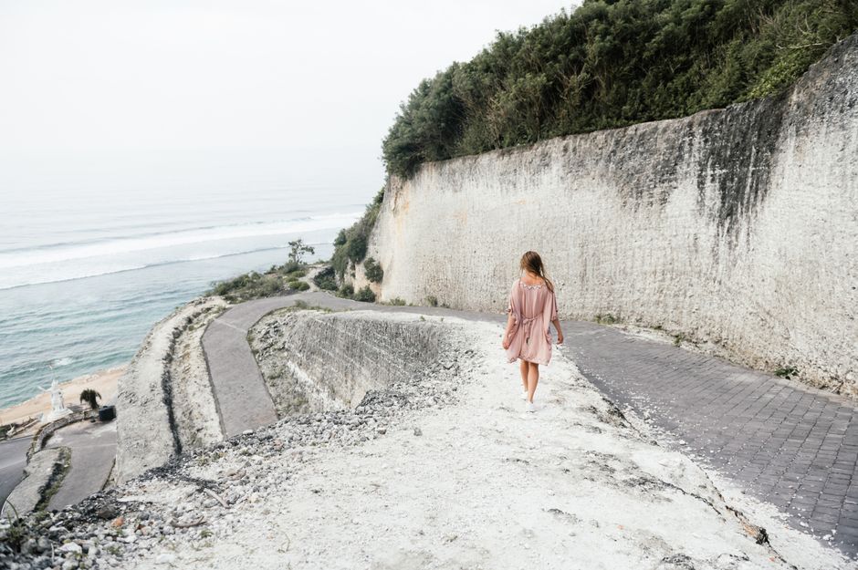 A woman strolling along a scenic pathway on a coastal cliff, embracing nature's beauty.