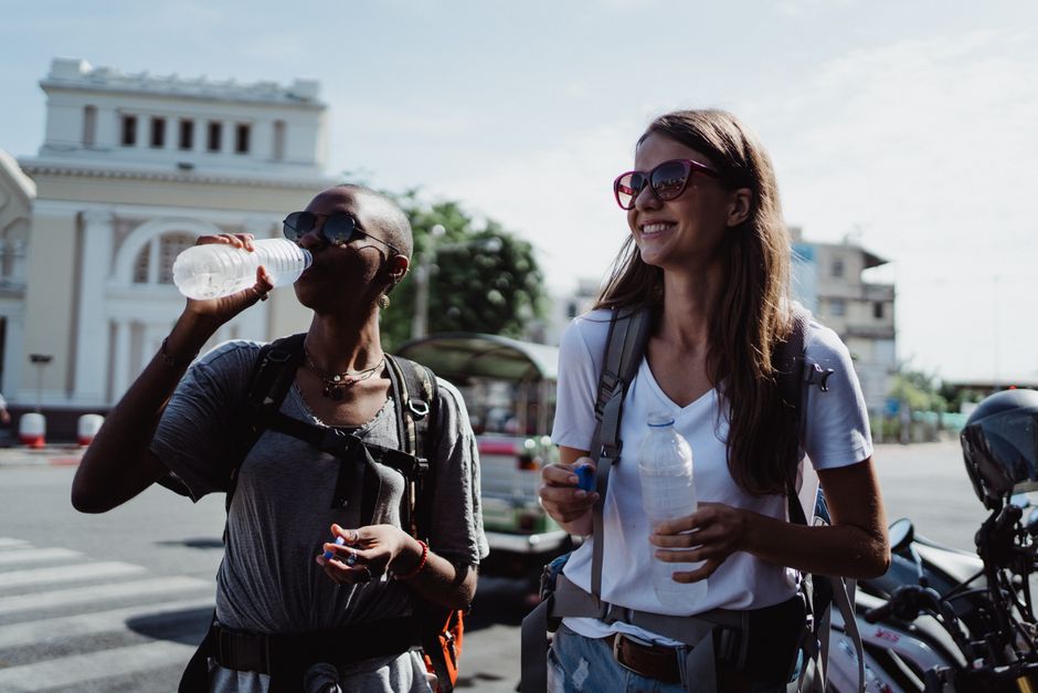 Two women backpackers sipping water while exploring the city streets under bright daylight.