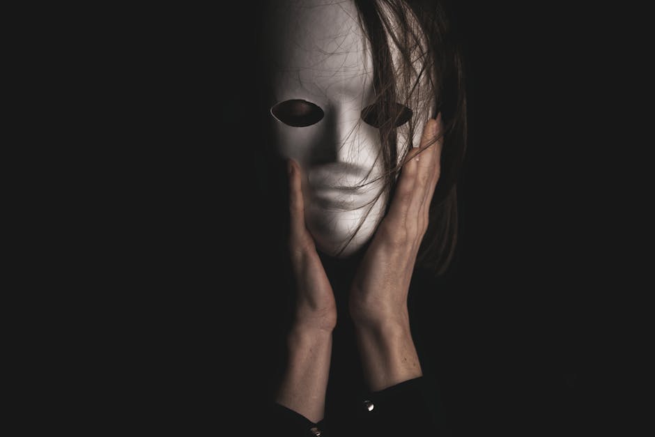 An eerie, dramatic portrayal of a person clutching a white mask, enveloped in darkness.