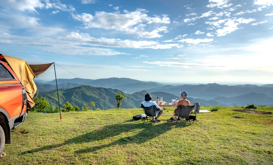 Couple enjoys a scenic campsite on hilltop with panoramic mountain views.