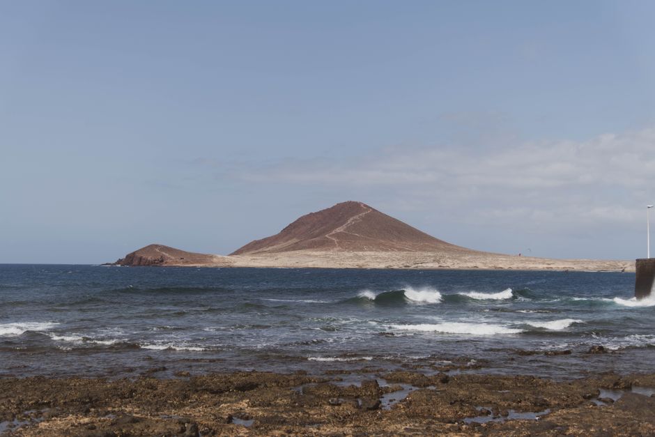 Stunning view of Montaña Roja from a rocky shoreline in Tenerife, capturing a serene seascape.
