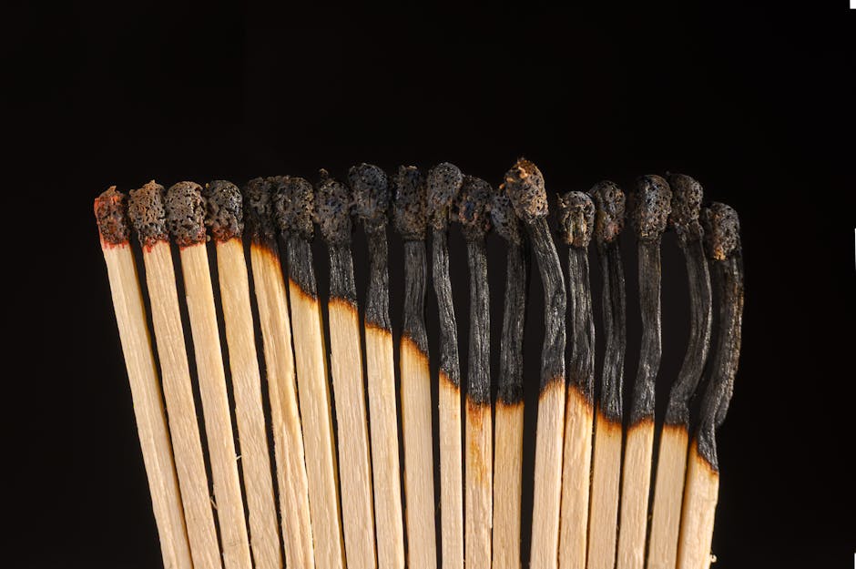 A row of burnt matches symbolizes burnout and exhaustion on a dark backdrop.