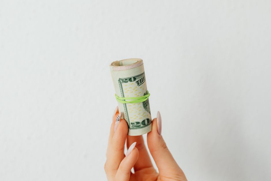Close-up image of a hand holding rolled US dollar bills on a white background.